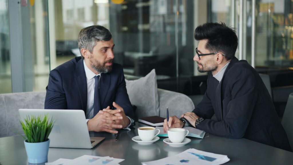 A salesperson and a buyer talking across a table with a laptop
